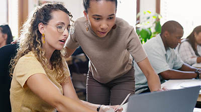 Two women working together on a computer while in an office 